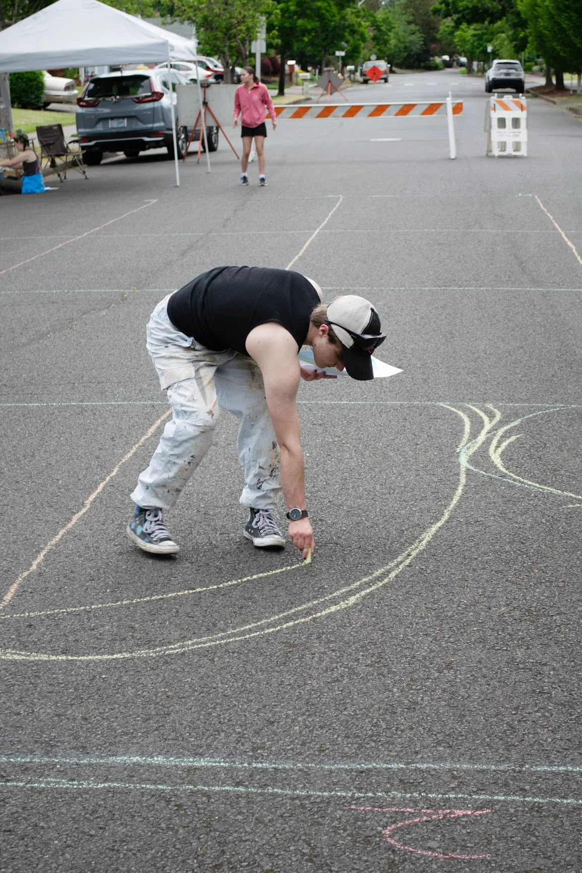 Everett bending over the closed-off street, transferring the design onto the asphalt in chalk with a printed reference sheet in hand.