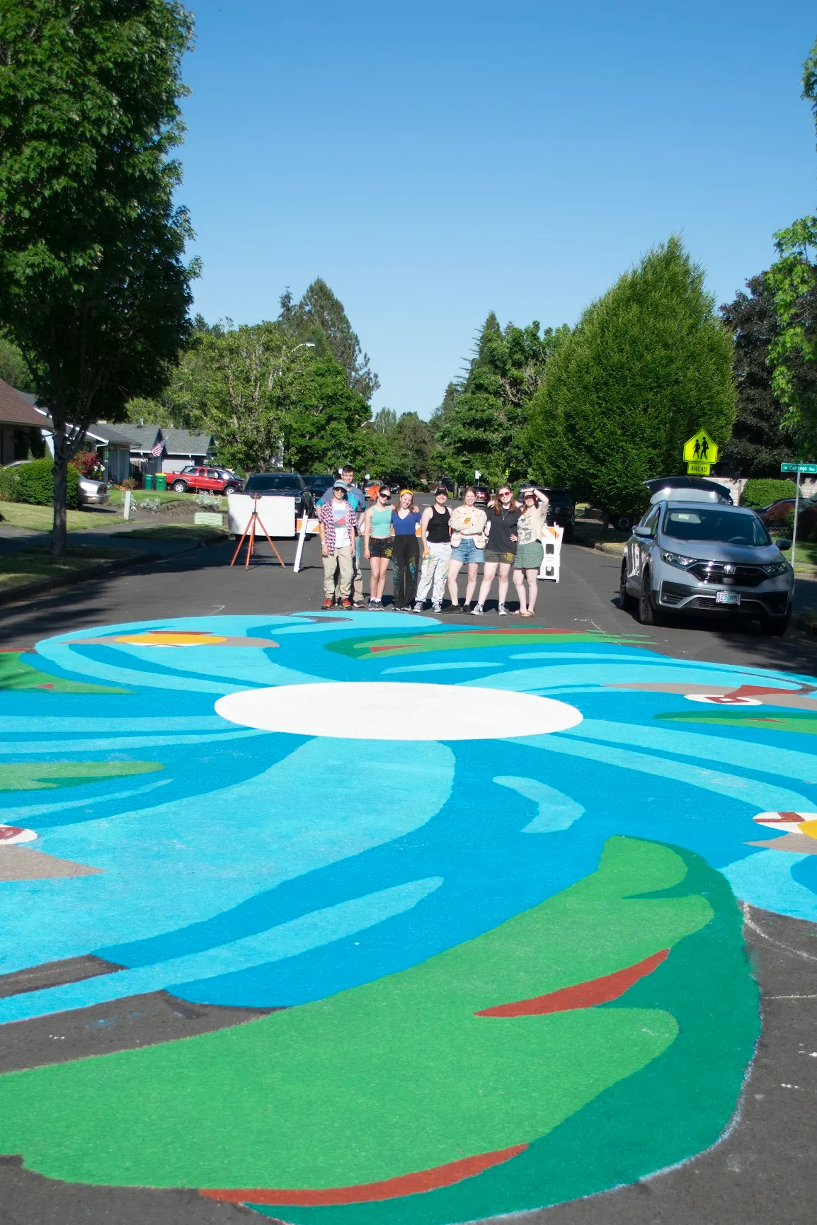 The volunteer team standing together at the edge of the finished mural, the painted swirl filling the street in front of them.
