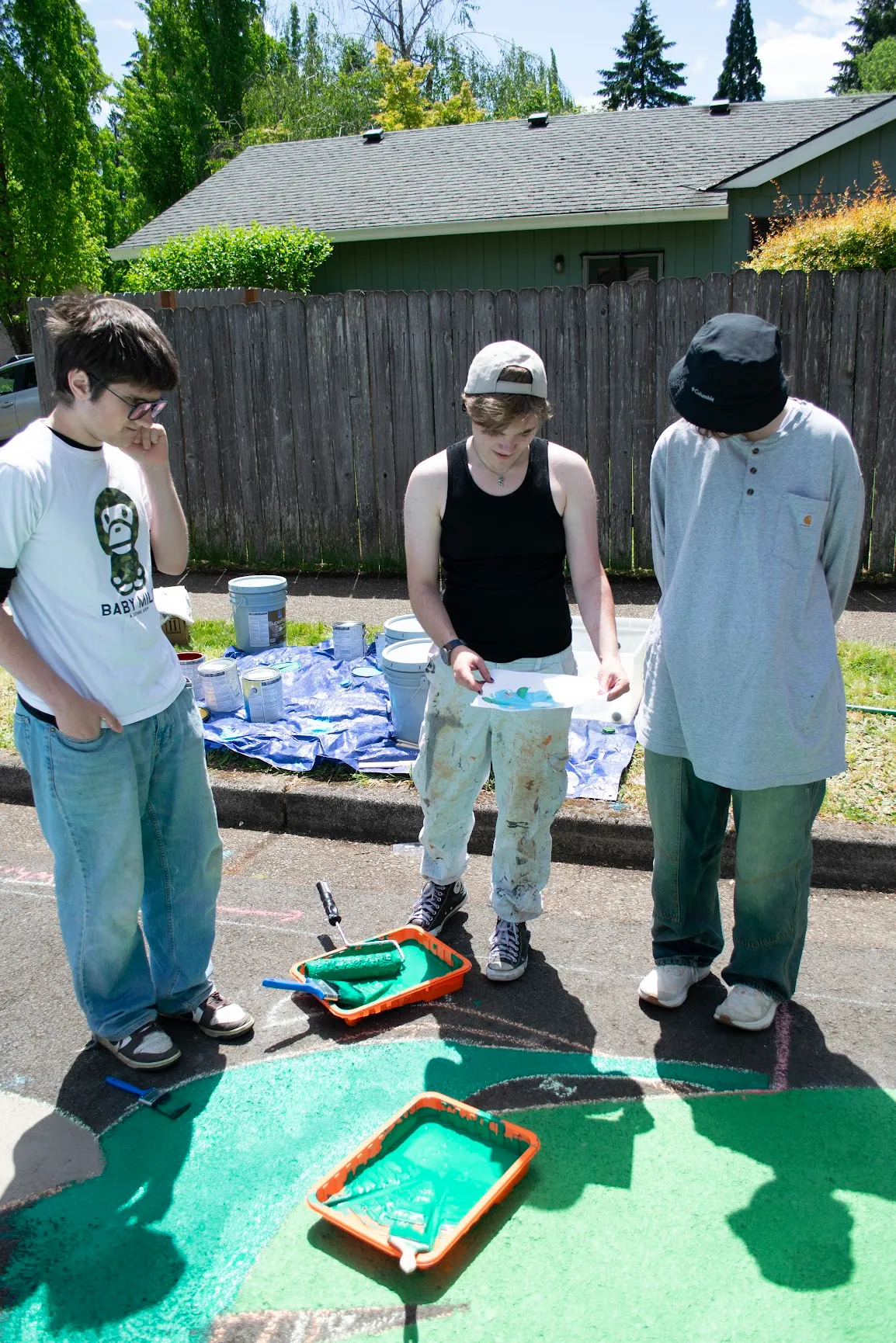Everett reviewing the design printout with two volunteers beside trays of green paint at the mural's edge.